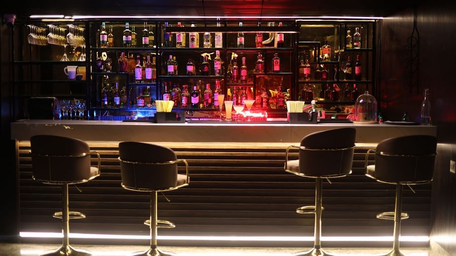 A stylish bar counter with glowing lights, featuring a wide selection of liquor bottles and two elegant stools, at Sarovar Portico, Sonipat.