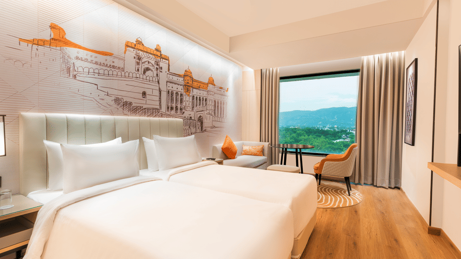 A twin bed hotel room at Sarovar Premiere Alwar with a view, a seating area, and a wall mural of a building.