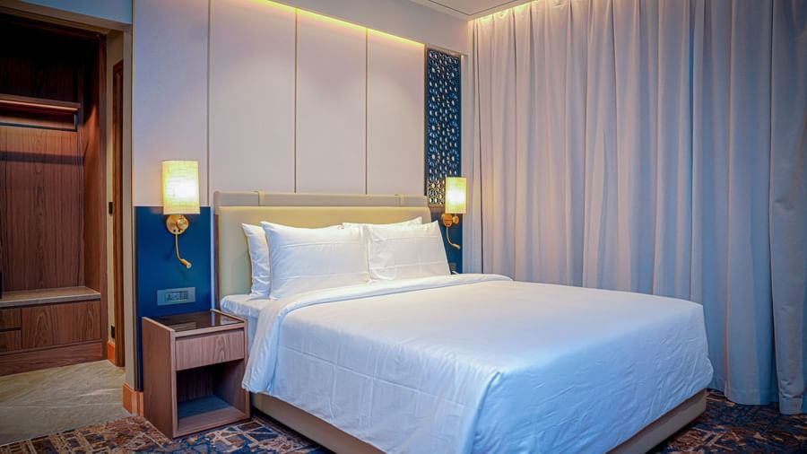 A double bed with plush pillows set against a beige headboard in a hotel room in Hargeisa - Serene Sarovar Premiere Hargeisa