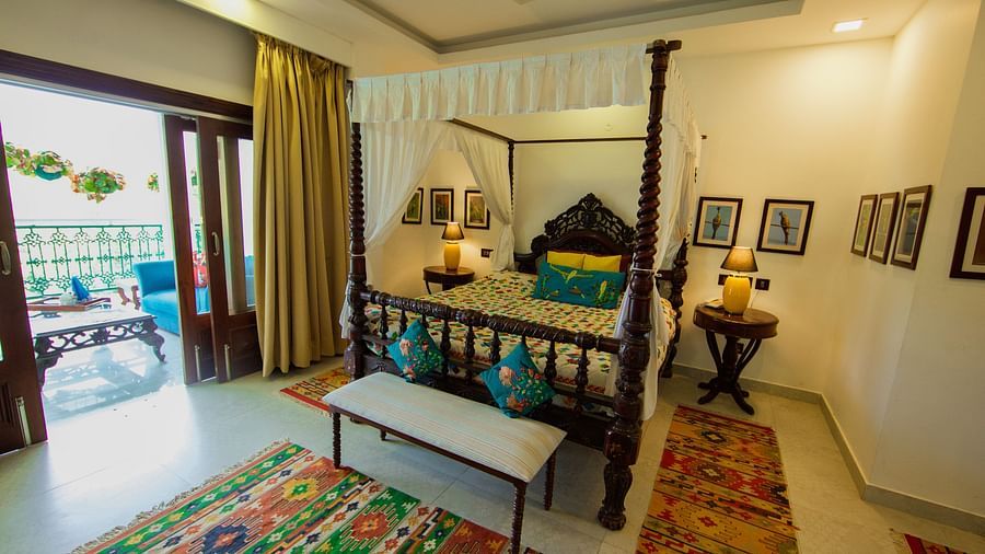 Bedroom with a four-poster bed, balcony overlooking a garden, and traditional Indian decor.