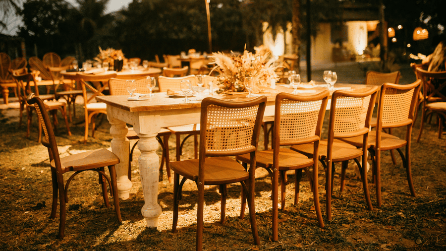 An outdoor dining area set up for an event with wooden tables and chairs under warm string lights.