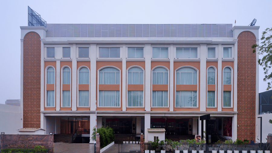Skywings Sarovar Portico Mathura hotel exterior daytime view with arched windows, cream facade, manicured entrance garden, and overcast sky backdrop.