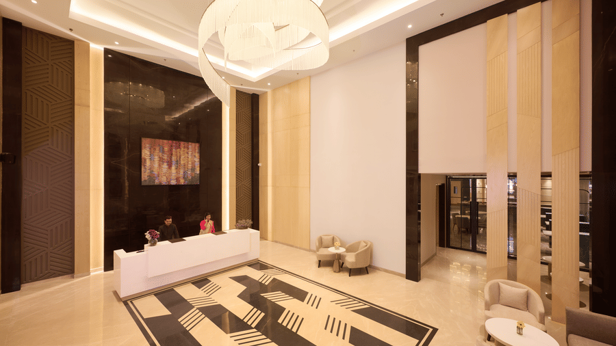 Skywings Sarovar Portico Mathura elegant lobby with geometric patterned flooring, golden ceiling lights, wooden wall panels, and modern elevator doors.
