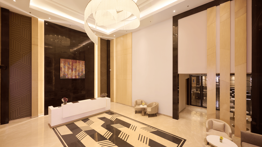 Skywings Sarovar Portico Mathura lobby seating area with gold vertical wall panels, white sofas, geometric flooring, and elegant chandelier overhead.