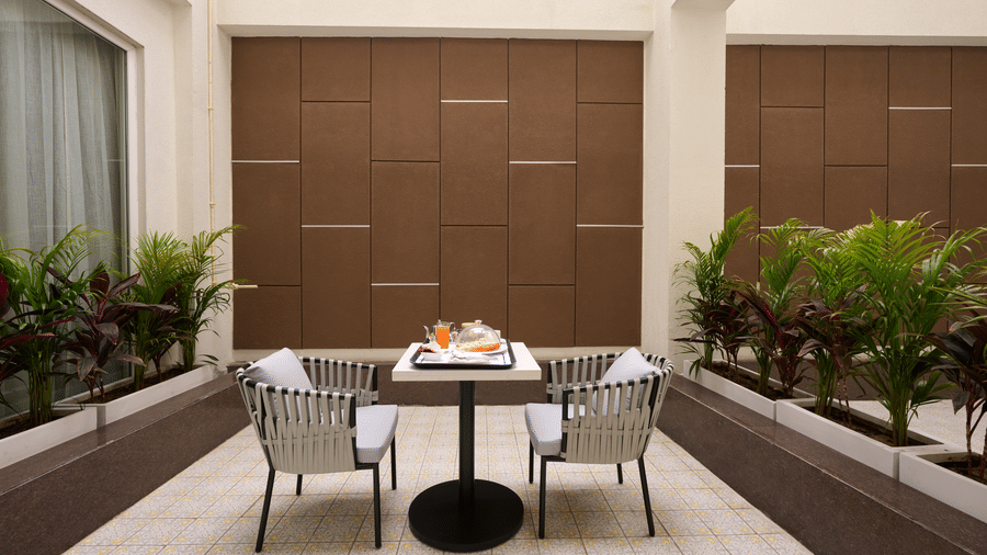 Skywings Sarovar Portico Mathura premium room private terrace with outdoor dining table, chairs, lush green plants, and wooden screen wall.