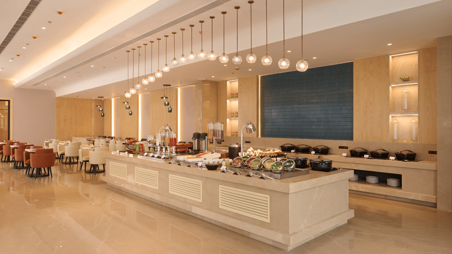 Skywings Sarovar Portico Mathura restaurant with marble buffet counter, pendant lights, blue wall art, dining seating area, and bright modern interiors.