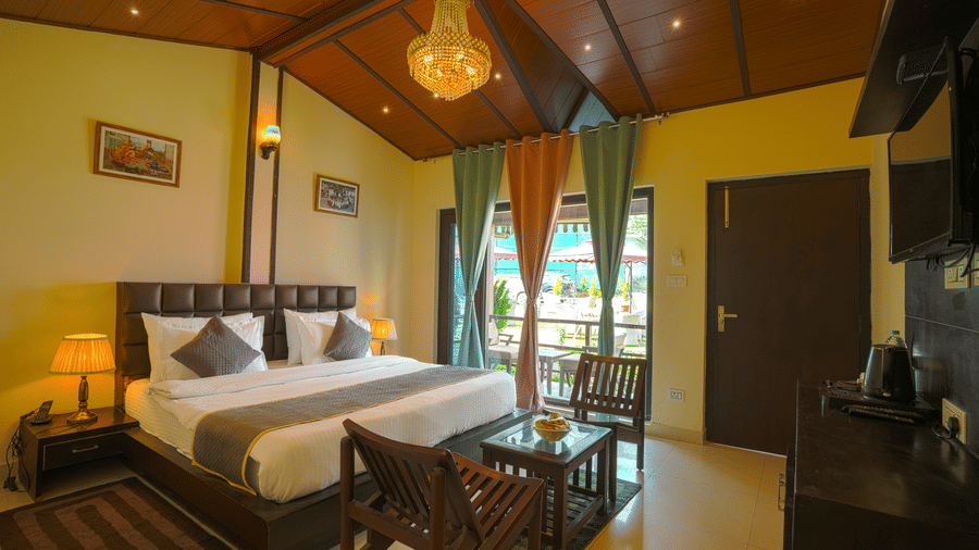 A room with a couple of chairs and a coffee table, a flat screen TV, a king bed with mattress and cushions, a chandelier | Sol Glow Resort, Nainital