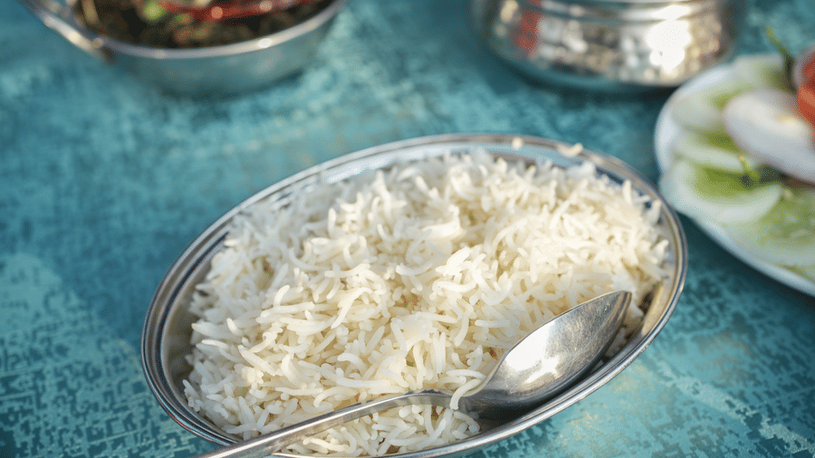 A close up shot of a bowl of rice in a stainless steel vessel with a spoon, near other dishes on the table | Sol Glow Resort, Nainital