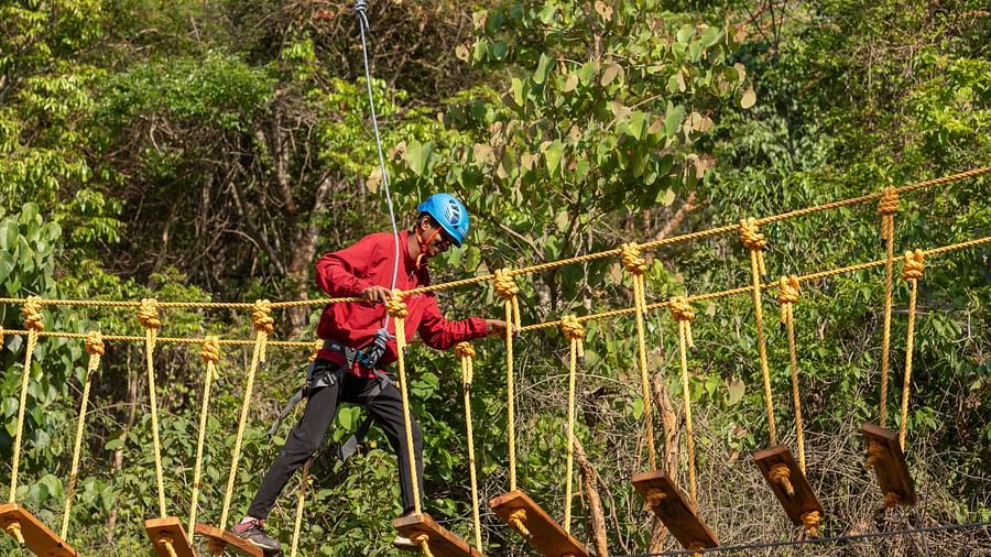 Image of a person maneuvering through a series of hanging tires on an adventure course. | Stone Wood Jungle Resort, Dandeli