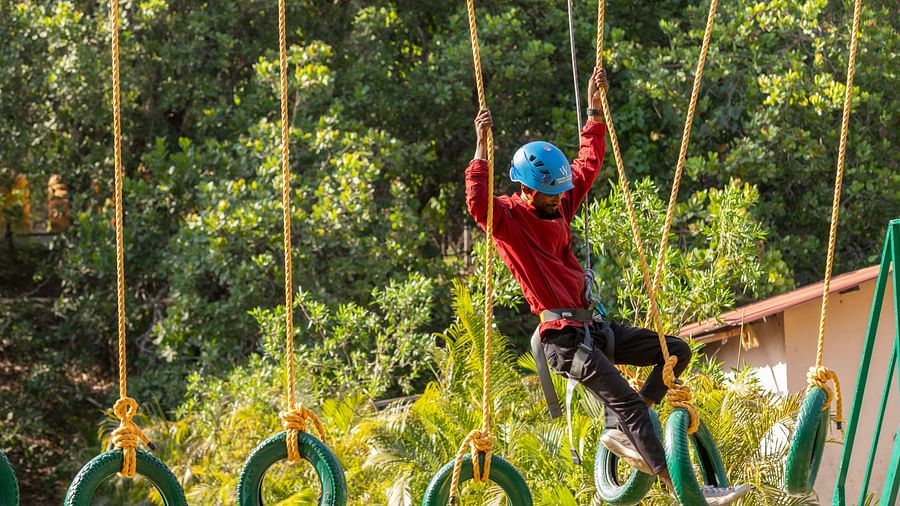 Image of a person crossing a rope bridge on an outdoor adventure course. | Stone Wood Jungle Resort, Dandeli