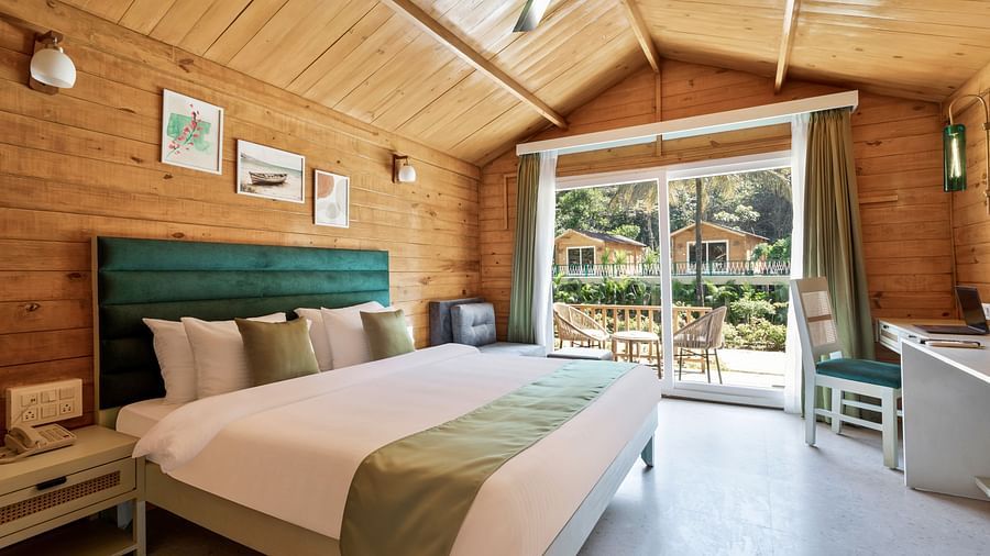 a double bed with pillows on it and entrance to the balcony in view inside one of the rooms - Stone Wood Jungle Resort, Dandeli