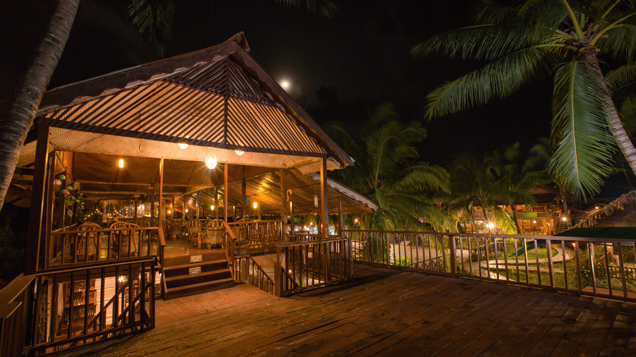 A structure with thatched roofing, illuminated with warm lighting at night.