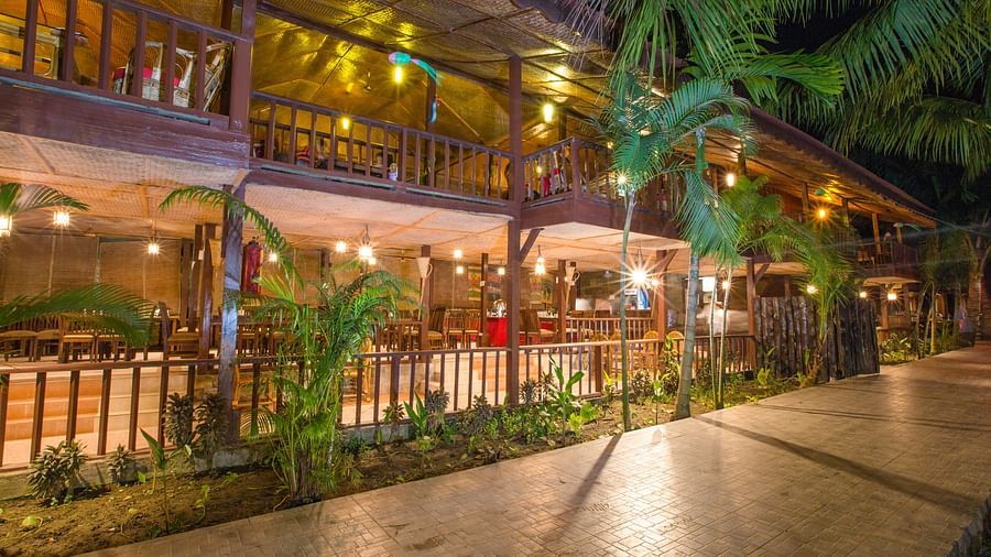 Tiled pathway with plants on the side and a brightly lit wooden building in the background