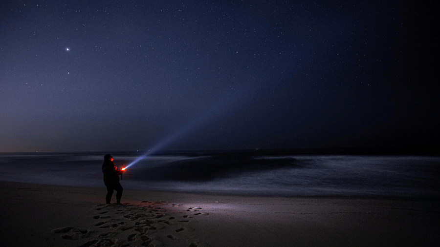A person holding a flashlight switched on roaming around the beach during the night.
