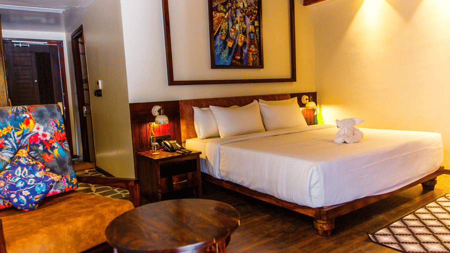 Interiors of a Port Blair water villa at Symphony Samudra Beachside Jungle Resort And Spa featuring a double bed, an arm chair, a coffee table, and painting hanging on a wall.