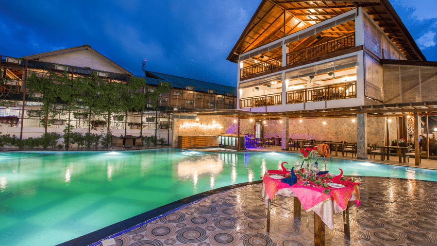 A table next to a swimming pool decorated with pink sheets and the facade of Symphony Summer Sand Beach Resort And Spa, one of the best resorts in the Andaman Islands, at the background.
