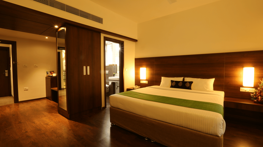 A spacious Executive Room featuring a bed with green runner, dark wood panelling, warm bedside lights, and wooden flooring at Temple Tree Hotel, Bangalore.