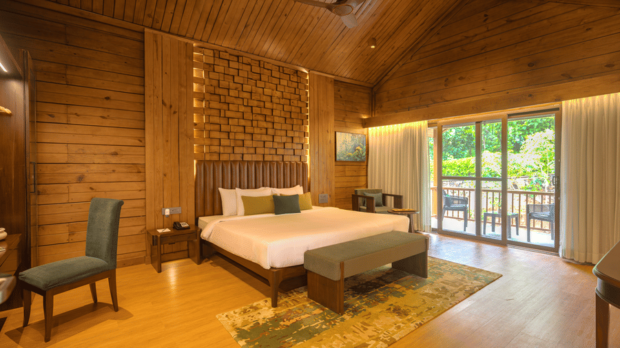 A room at The Ananta Udaipur, featuring a large bed, spreads, pillows, sofas, a window, and wooden wall.