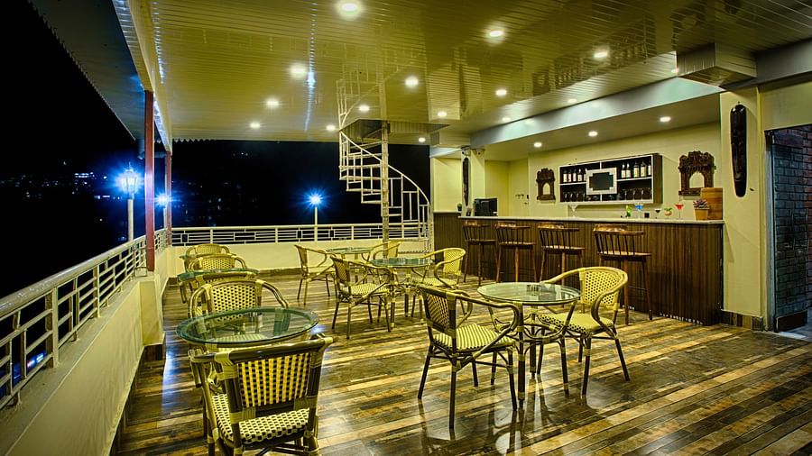 a bar area with sky view decorated with soft lighting with proper seating arrangement and a bar counter on the left - The aryan regency