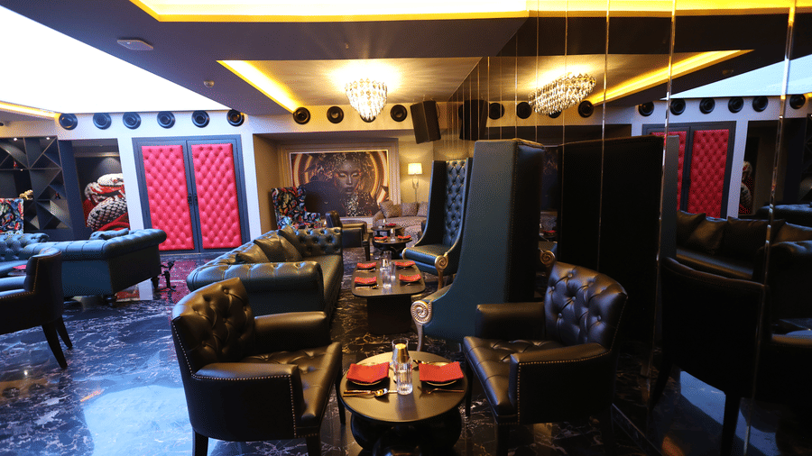 Dark, plush lounge at The Beatle Hotel, Powai, with black seating, red accents, and a glittering chandelier.