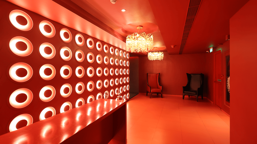 Long, vibrant red hallway at The Beatle Hotel, Powai, with a repeating circular pattern on the side wall and a fixture at the end.