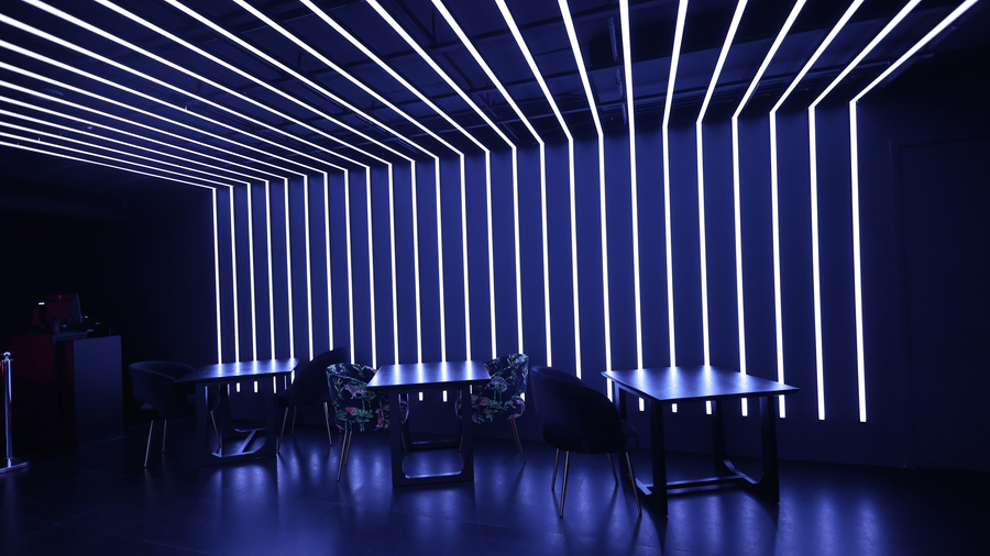 Club area at The Beatle Hotel, Powai. Vertical blue-white LED strip lights create a dynamic, segmented wall pattern near dark tables and chairs.