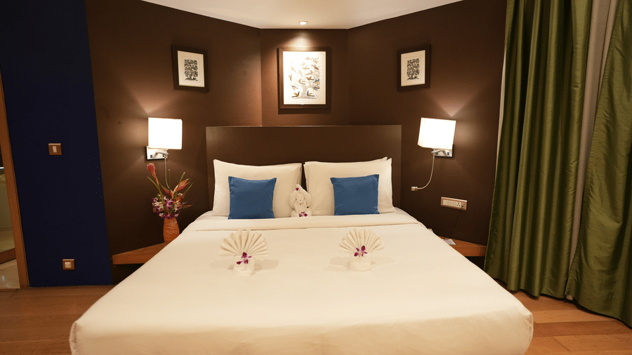 Suite room at The Beatle Hotel, Powai featuring a double size bed, with bedside table with lamps on either side, and a huge curtain on one side.