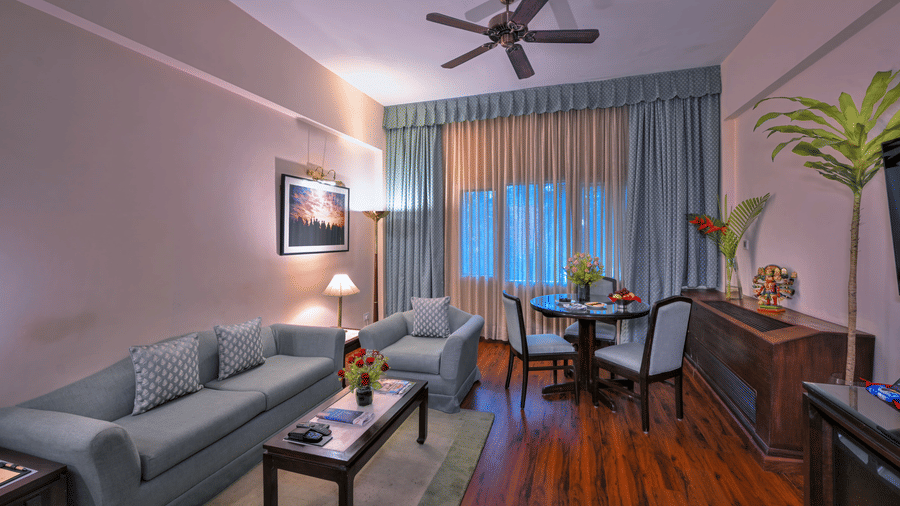 A room with sofas, spreads, pillows, a fan, and windows at The Clarks Varanasi.