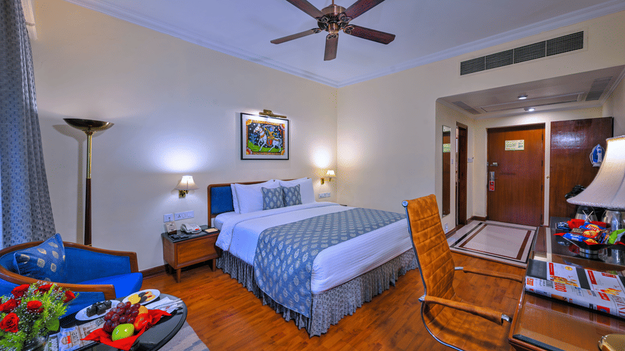 A room with a large bed, spreads, pillows, a fan, and windows at The Clarks Varanasi.