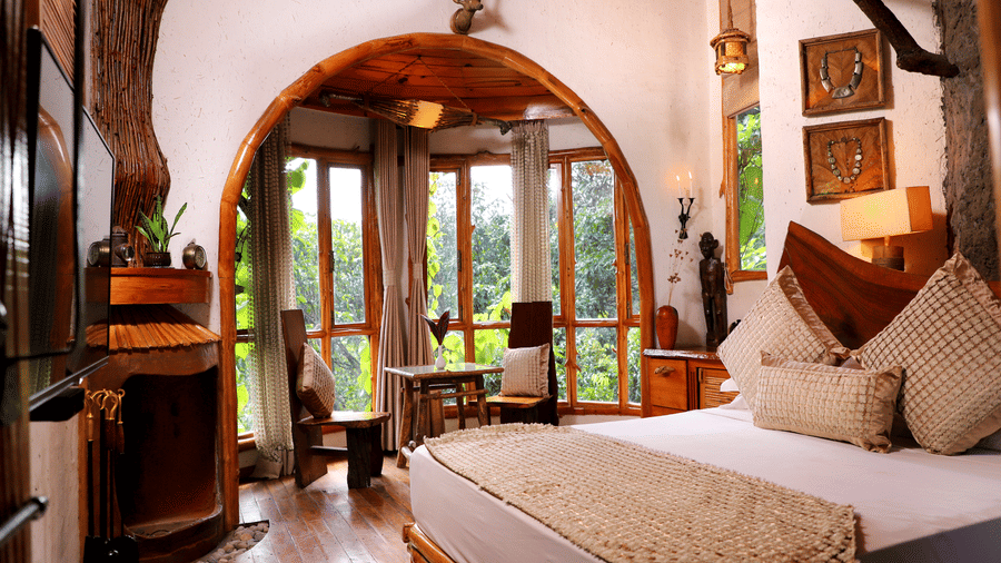 A bedroom with  a queen bed and an arc pass through leading to the sitting area overlooking the greenery at  The Den Corbett Resort and Spa.
