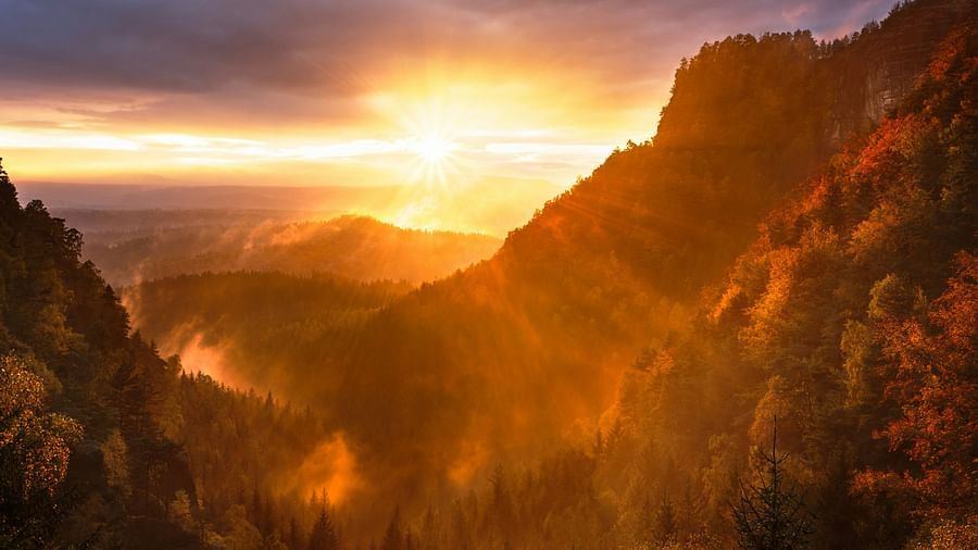 An image of sunrise over the mountains, with vibrant orange and yellow hues peeking between the peaks