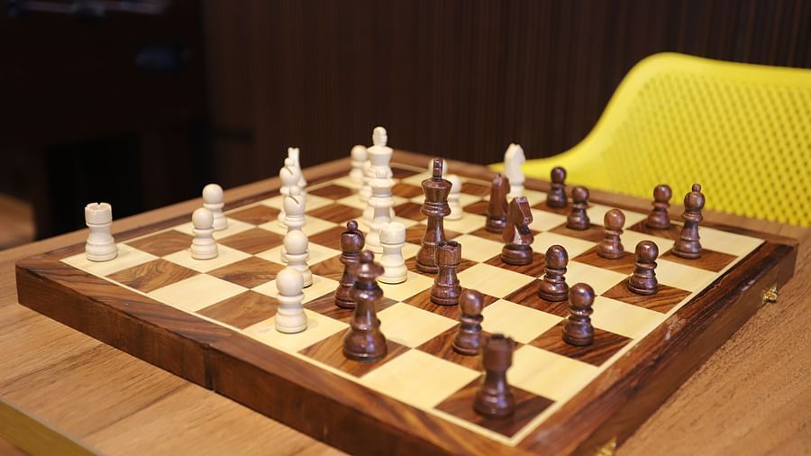 A wooden chess set with white and dark pieces arranged on a board, possibly located in a recreational area at The Gaurs Sarovar Premiere.