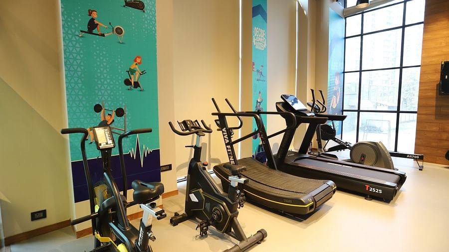 A gym area at The Gaurs Sarovar Premiere, featuring treadmills, weightlifting equipment, and a mirrored wall.