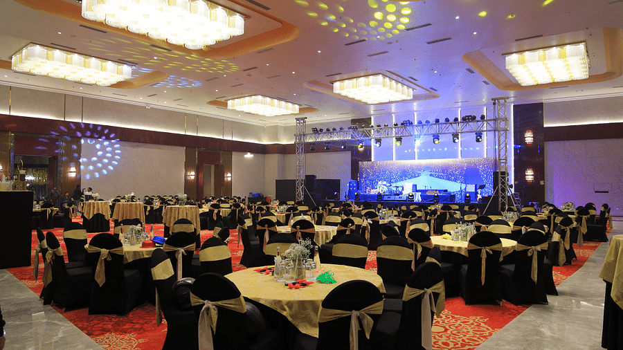 A decorated banquet hall at The Gaurs Sarovar Premiere with a stage, lighting, and round tables set for an event.