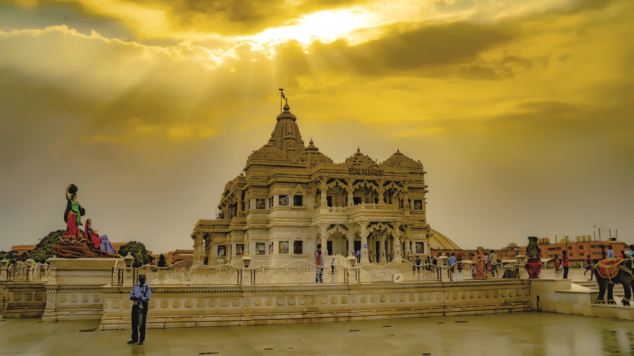 Stunning temple under a dramatic golden sky with sun rays shining through clouds, featuring intricate carvings, statues, visitors, and a polished courtyard.