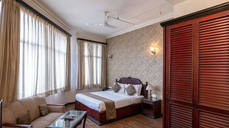 An image of a well-furnished bedroom with two large windows that have curtains drawn  - The Lindsay