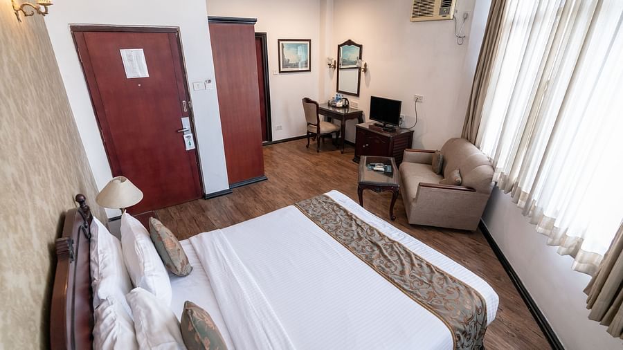 An image of a bedroom that has king size bed, a sofa, tables, cupboard, flat TV screen, and some photo frames  - The Lindsay