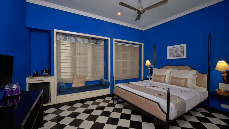 Vibrant blue hotel room at the Old Court House by Abad, with a four-poster bed and checkered floor, perfect for a stay near Fort Kochi beach.