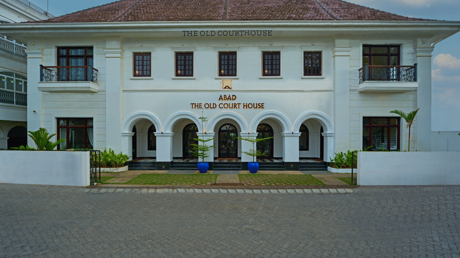 A colonial-style white building with a symmetrical facade, arched entryway, and a sign reading The Old Court House above the entrance
