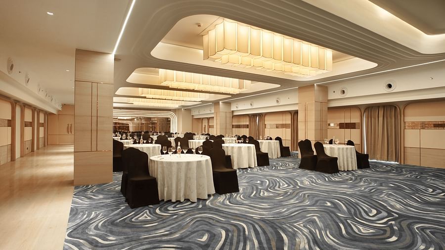 Modern ballroom setup with round tables dressed in white, paired with dark chairs. Unique curved ceiling design and patterned carpet - The Orchid Hotel, Chandigarh