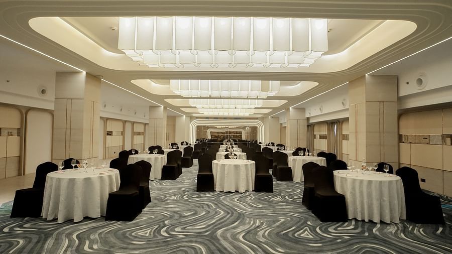 Spacious event venue with round tables covered in white cloths and black chairs. Bright overhead lighting and patterned floor - The Orchid Hotel, Chandigarh