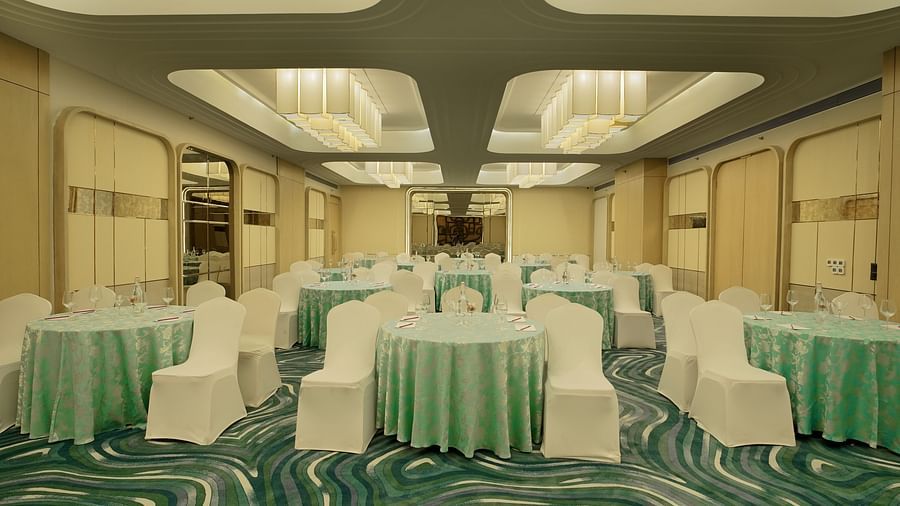 Banquet room with round tables draped in light green, surrounded by white chairs. Patterned carpet and soft lighting - The Orchid Hotel, Chandigarh