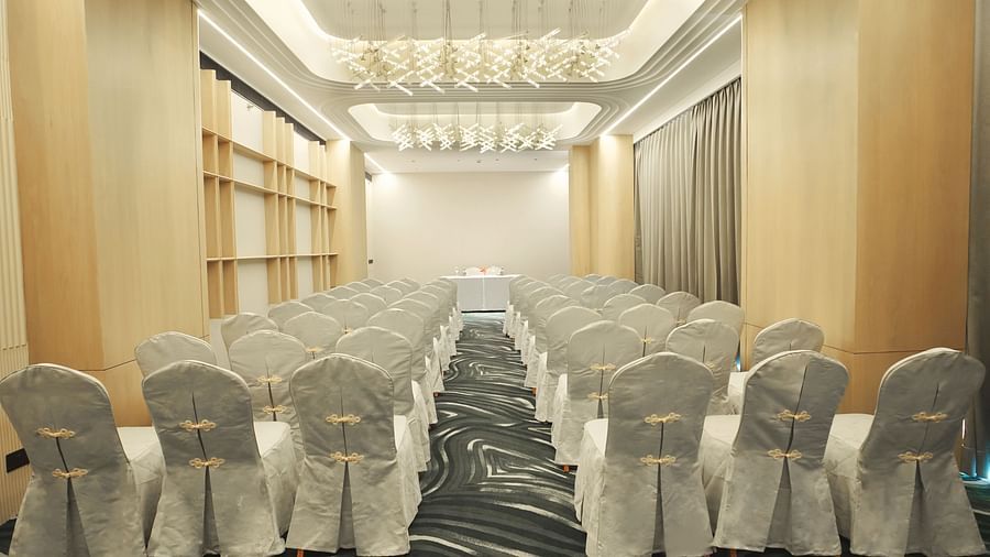 Long view of a conference room with rows of white-covered chairs facing forward. Patterned carpet and modern ceiling lights - The Orchid Hotel, Chandigarh