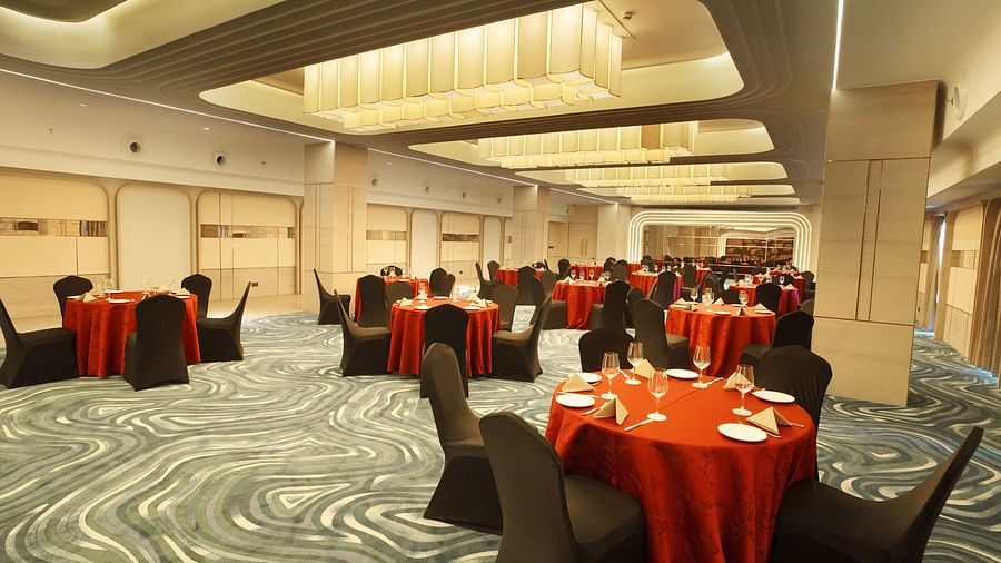 Festive banquet hall with round tables dressed in red, accompanied by black chairs. Patterned floor and warm lighting - The Orchid Hotel, Chandigarh