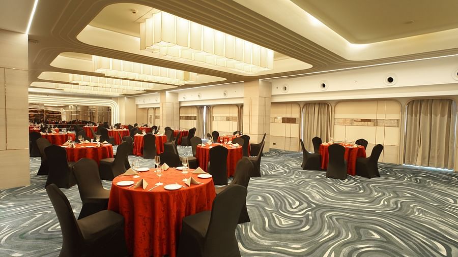 Inviting event space with round tables featuring red linens and black chairs. Patterned carpet and subtle lighting - The Orchid Hotel, Chandigarh
