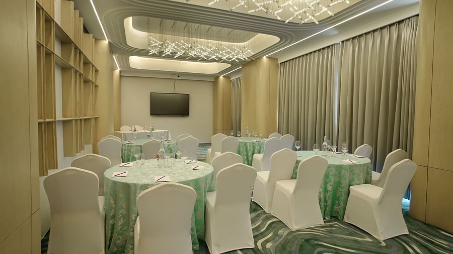 Function room with round tables featuring teal linens and white chairs. Patterned carpet and contemporary lighting - The Orchid Hotel, Chandigarh