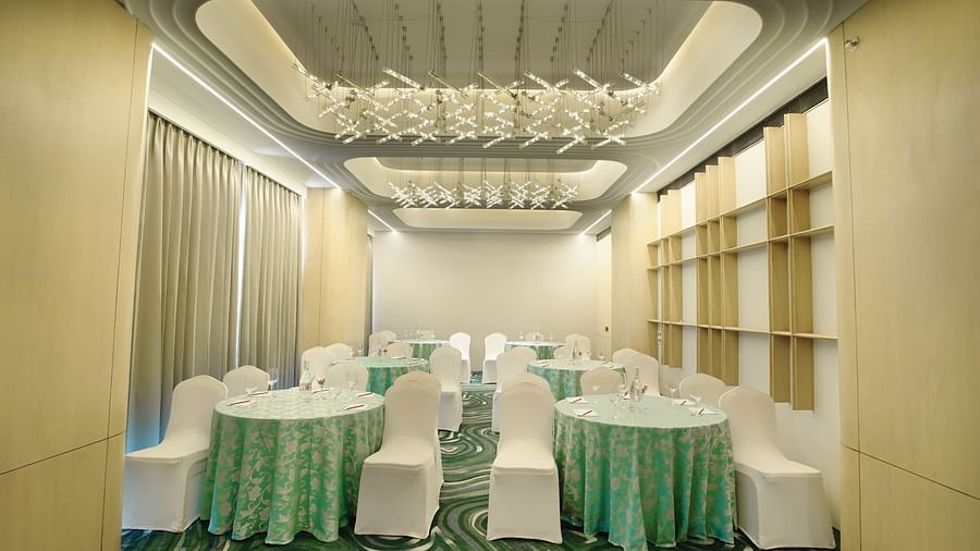 Banquet hall with round tables dressed in teal, accompanied by white chairs. Patterned floor and window drapes - The Orchid Hotel, Chandigarh