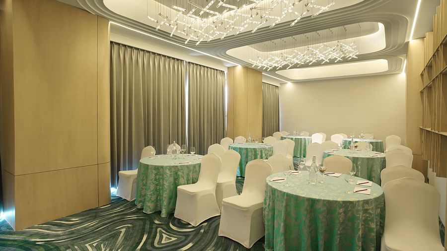 Event room with round tables draped in teal, surrounded by white chairs. Patterned carpet and modern ceiling lights - The Orchid Hotel, Chandigarh