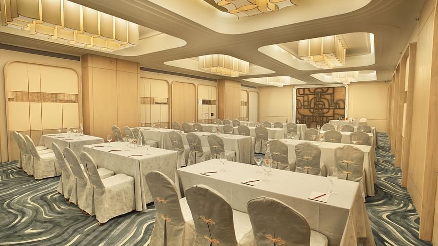 Brightly lit room with rectangular tables covered in white linens and white chairs. Patterned floor and modern ceiling - The Orchid Hotel, Chandigarh