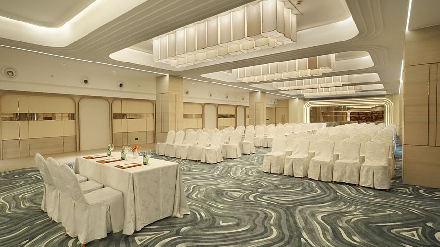 Event hall with rows of white-covered chairs facing a table with white linens. Patterned carpet and modern ceiling lights - The Orchid Hotel, Chandigarh